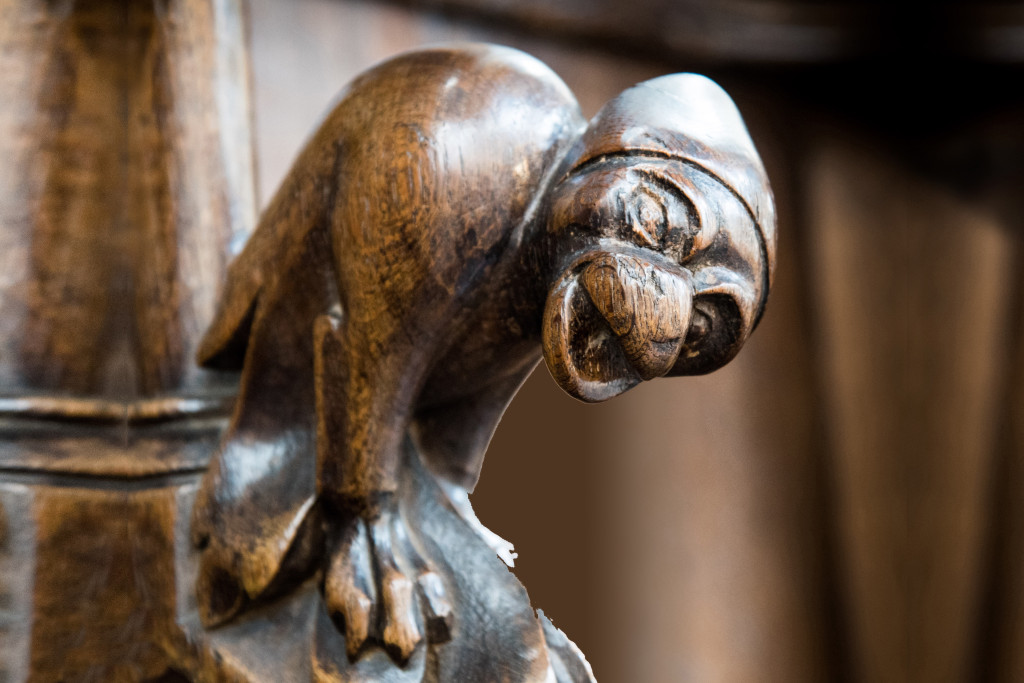 Aan de doopvont in de Sint-Jacobskerk in Luik hangt een griezelig lachende apenkop, die verwijst naar een satirisch verhaal over een bisschop. Griezelig lachend aapje, detail van een doopvont