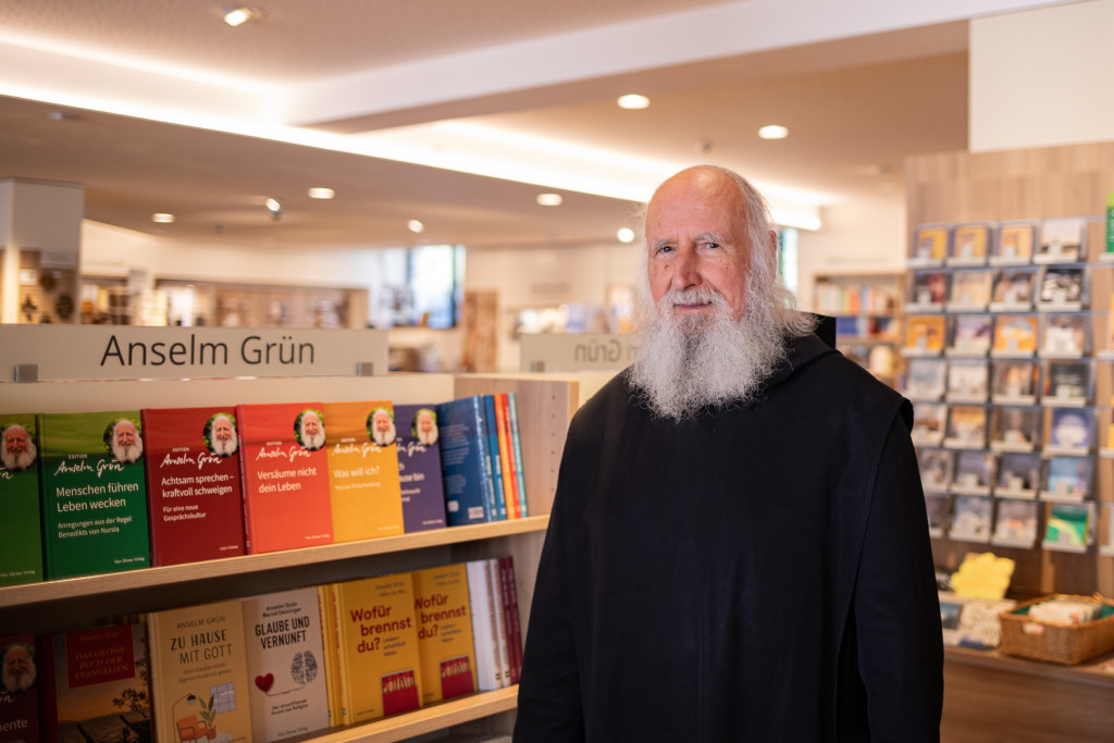 Pater Anselm Grün bij een boekenstand vol boeken met zijn naam erop.