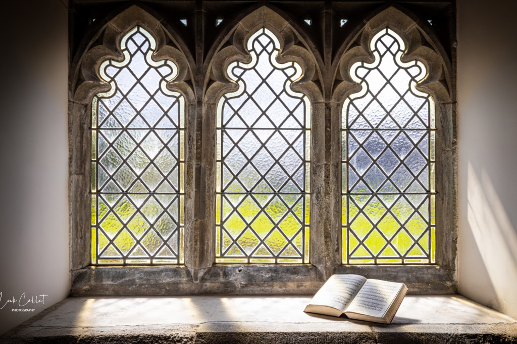 Luk Collet ging op zijn pelgrimsroute elke kerk binnen en nam er uitgebreid foto's. 'Voor een pelgrim onderweg is een kerk meer dan een tussenstop.' Sobere glasramen in een romaans kerkje in Cornwall, met een open Bijbel voor het raam.