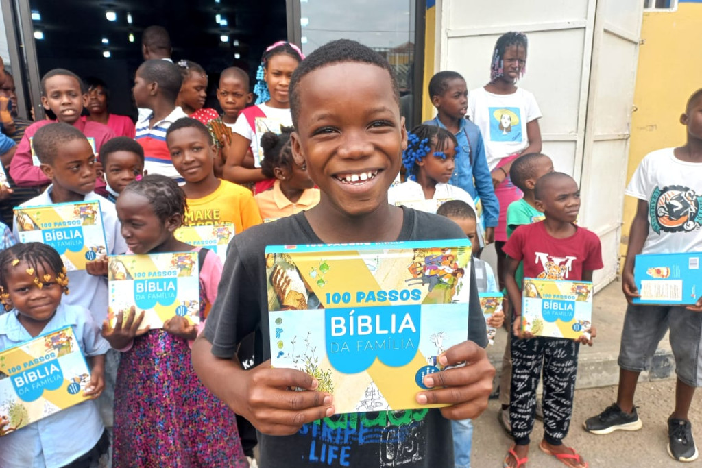 Een jongetje in Angola toont een exemplaar van de Family Bible met een grote glimlach op zijn gezicht.