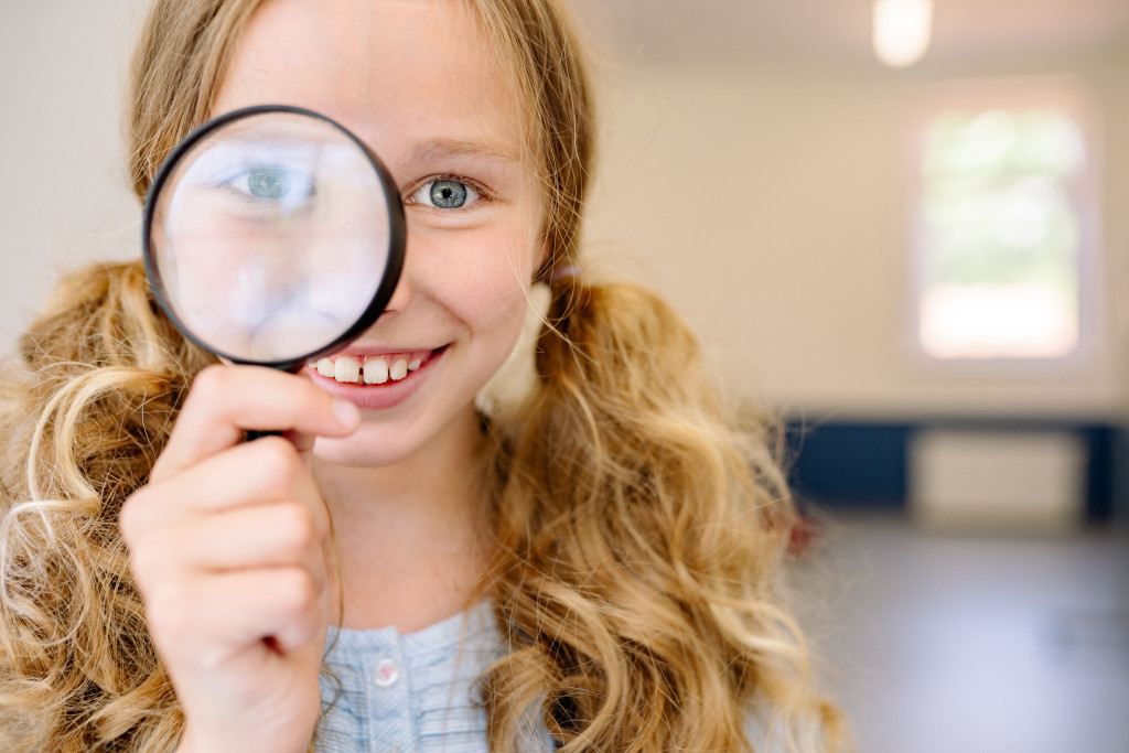 Meisje met guitige glimlach kijkt door vergrootglas. Haar oog is grappig uitvergroot.