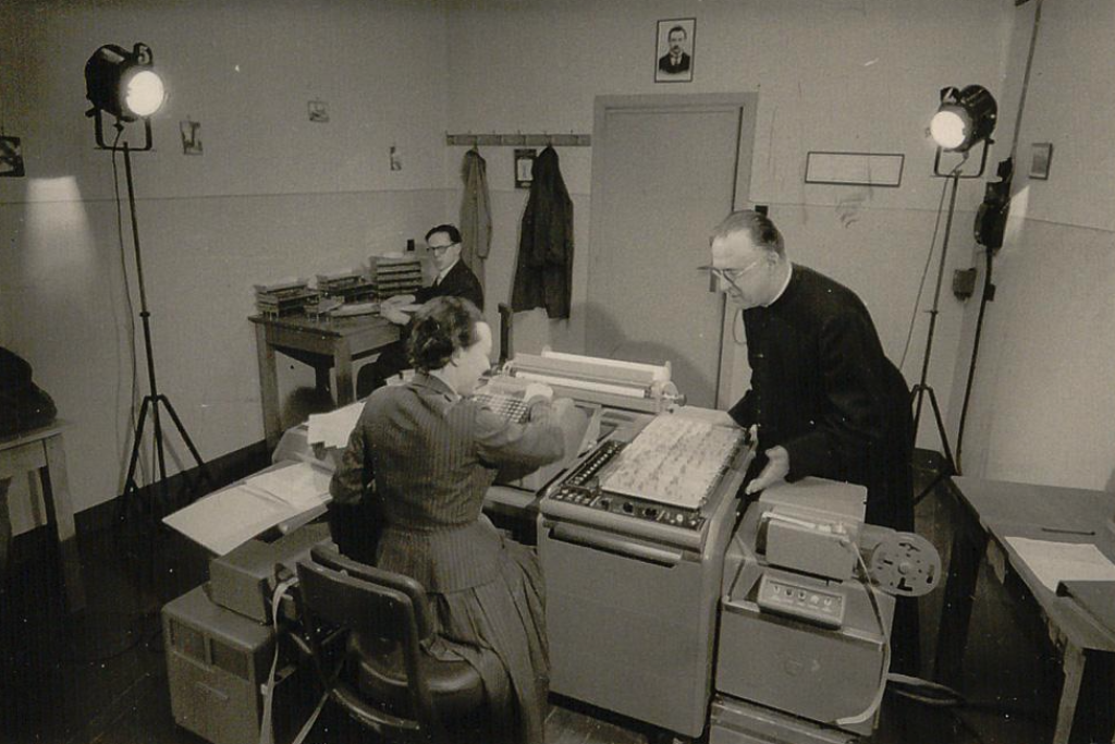 Georges Lemaître bij de Burroughs E101, de eerste computer van de Leuvense universiteit, in mei 1959. Links zit wetenschappelijk assistente Andrée Bartholomée; ook professor Louis Bouckaert is aanwezig. De computer werd persoonlijk door Lemaître aangekocht. 