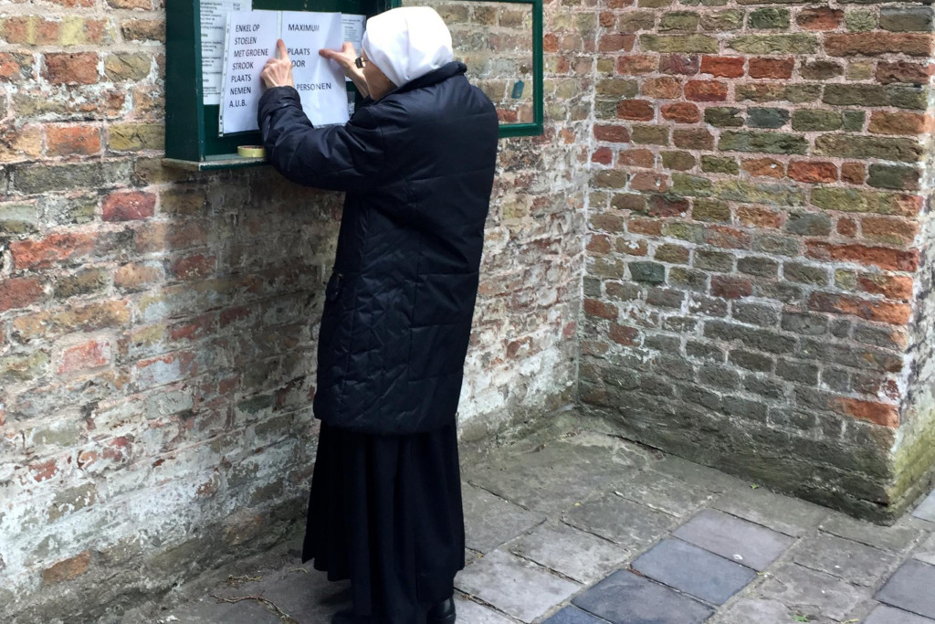 Een zuster hangt een blad met richtlijnen uit aan de Begijnhofkerk in Brugge.