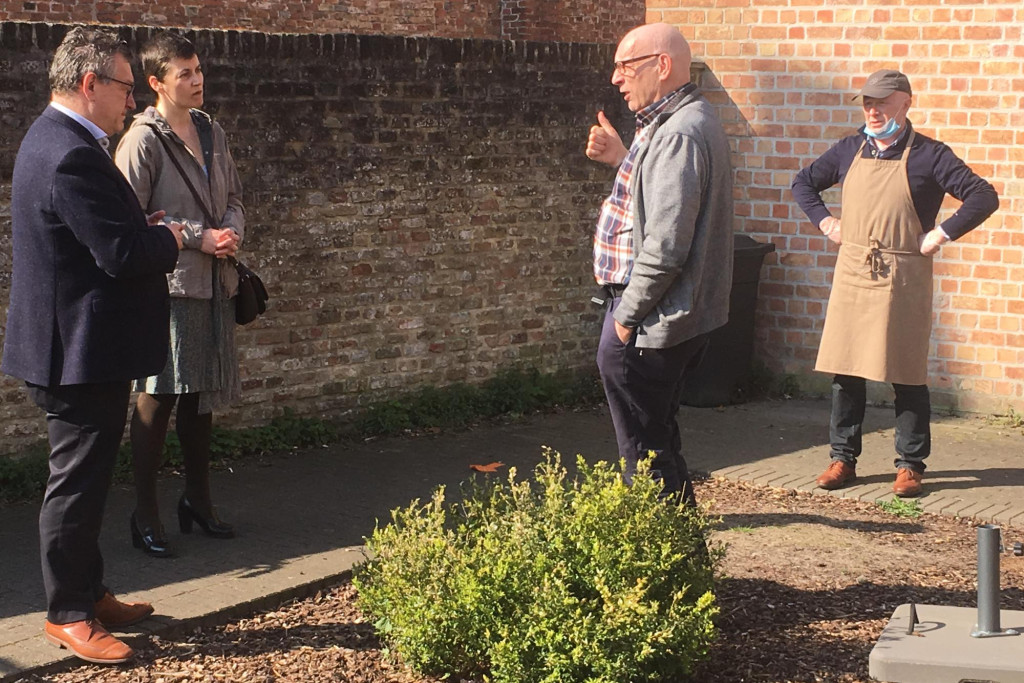Priester Antoon Vandeputte geeft uitleg aan burgemeester Dirk De fauw en gemeenteraadslid Doenja Van Belleghem over de afhaalmaaltijden-actie van Open Balie