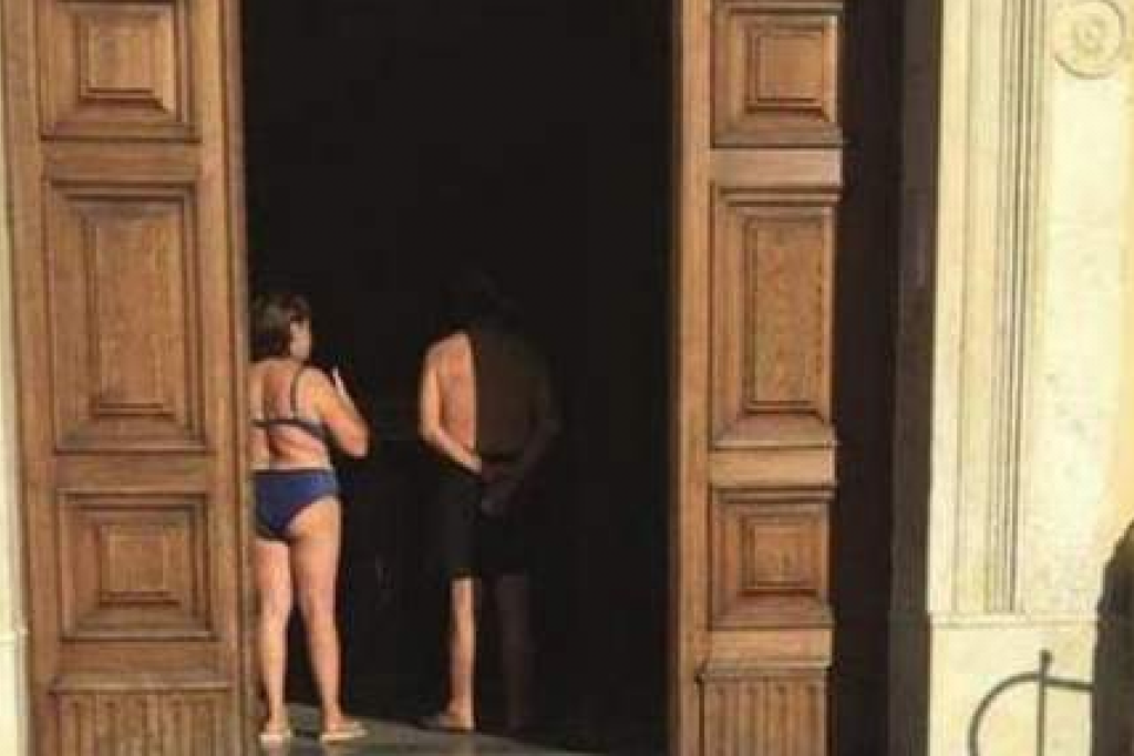 Schaars geklede toeristen gaan een kerk binnen in Villammare.