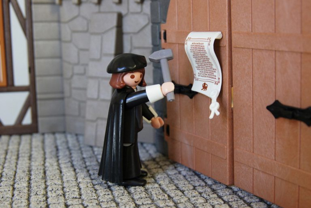 Een Lutherfiguur van Playmobil spijkert zijn 95 stellingen tegen de poort van de kerk in Wittenberg.